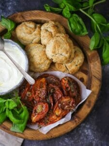 Tomato "Shortcake" with Whipped Ricotta ingredients on a round wood board with basil scattered around.