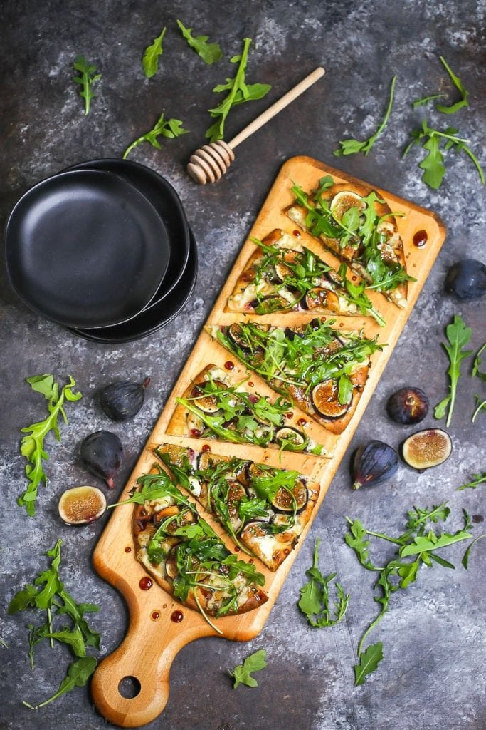 Fig, blue cheese, and arugula flatbread sliced and served on a wooden cutting board and drizzled with honey balsamic vinaigrette.
