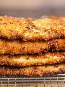 Close up of breaded chicken breasts stacked and cooling on a wire rack.