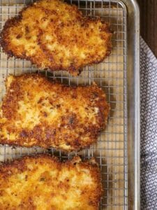 Close up of breaded chicken breasts cooling on a wire rack.