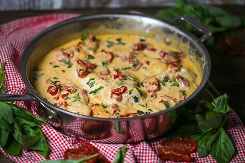 Close up of chicken with creamy sun-dried tomato sauce simmering in a saute pan sprinkled with fresh basil.