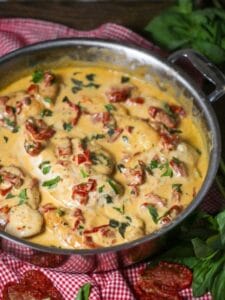 Close up of chicken with creamy sun-dried tomato sauce simmering in a saute pan sprinkled with fresh basil.