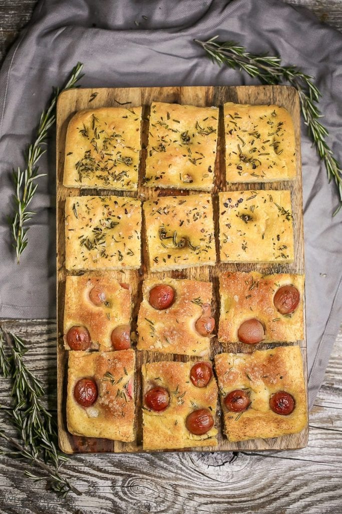 Overhead shot of sweet and savory Fluffy Focaccia Bread, cut into squares with sprigs of rosemary on the side.