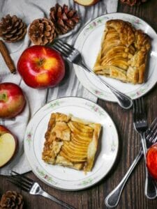 Square slices of Caramel Apple Slab Pie on plate with red apples and pinecones scattered around.