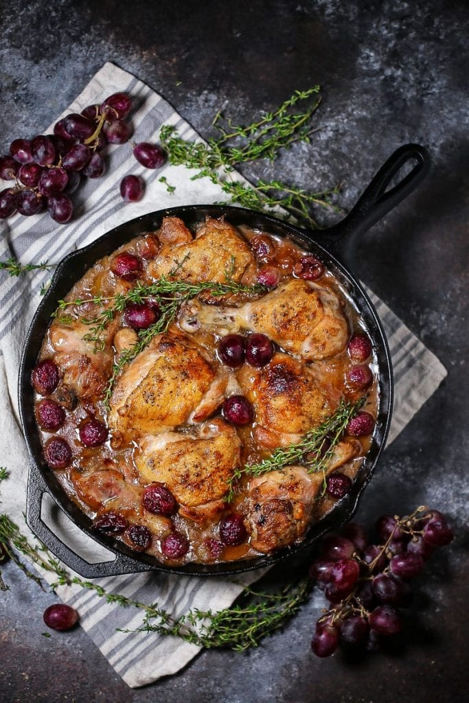 Braised Chicken with Grapes in a cast iron skillet with sprigs of thyme and grapes scattered around.