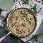 Overhead shot of creamy mushroom risotto in a silver saute pan with sprigs of thyme and mushrooms slices scattered around.