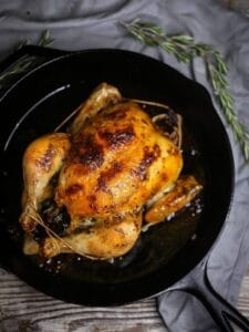 Overhead shot of perfect roast chicken in a cast iron pan with rosemary scattered around.