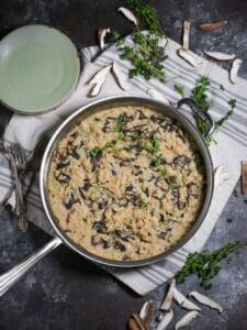 Overhead shot of creamy mushroom risotto in a silver saute pan with sprigs of thyme and mushrooms slices scattered around.