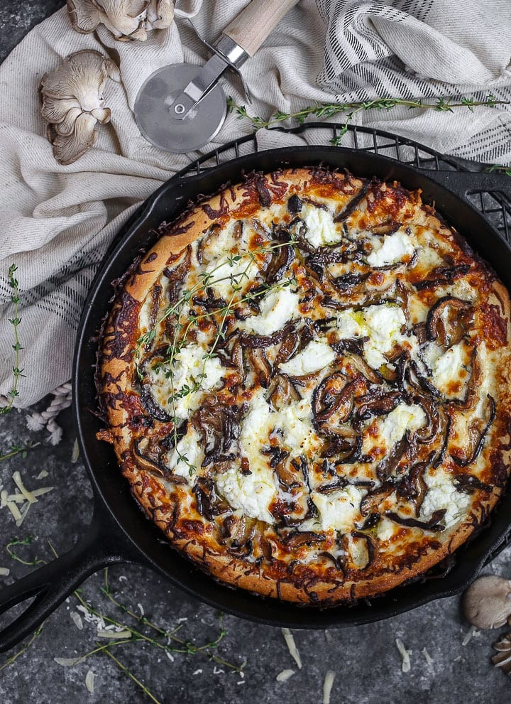 White mushroom pizza baked in a cast iron skillet, dolloped with ricotta and scattered with thyme sprigs.