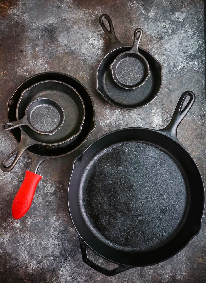 Different size cast iron skillets arranged on a table, one with a red handle protector.