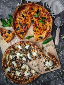 White mushroom and classic skillet pizzas on a cutting board with slices cut out, scatter with herbs and a pizza cutter laying on the table.
