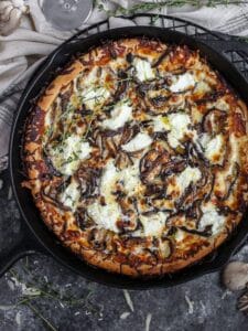 White mushroom pizza baked in a cast iron skillet, dolloped with ricotta and scattered with thyme sprigs.