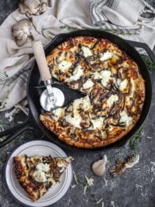 White mushroom pizza served in a cast iron skillet with a slice cut out and served on a small plate.