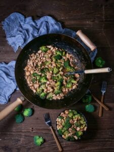 A serving of Chicken and Broccoli Stir-Fry in a black bowl with a few forks on the table and the wok with the stir-fry placed above.