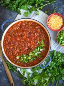 Overhead shot of Hearty Vegetarian Chili. The chili is in a large pot sprinkled with herbs and cheese and cilantro scattered around.