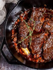 Irish Whiskey Braised Short Ribs in a cast iron dutch oven with thyme sprigs scattered on top.