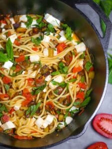 Overhead shot of roasted eggplant pasta in a cast iron dutch oven garnished with fresh basil.