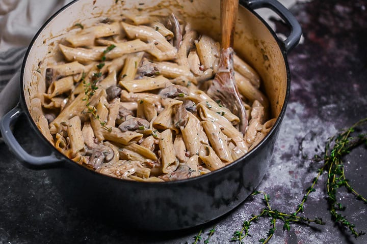 Creamy Goat Cheese Pasta with Chicken and Mushrooms in a blue enamled dutch oven with a wooden spoon in the pot to stir and a few thyme sprigs scattered around.