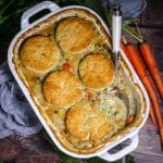 Vegetable Pot Pie with Biscuit Topping in a white baking dish with a portion scooped out with a spoon and carrots on the side.