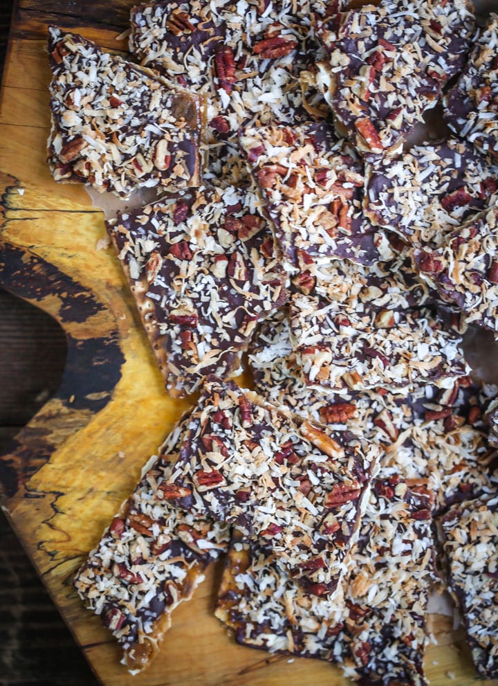 Toffee Matzo Brittle (aka matzo crack), is topped with toasted coconut and pecans is piled on top of a wood board.