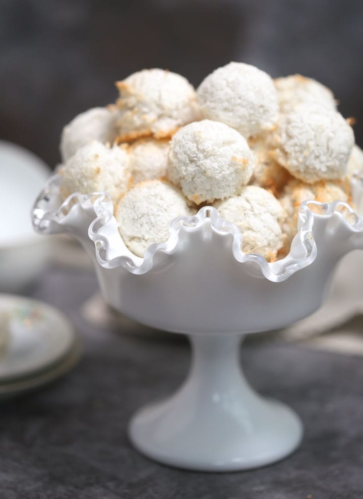 A pile of coconut macaroons in a white footed, fluted bowl.