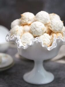 A pile of coconut macaroons in a white footed, fluted bowl.