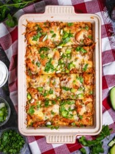 Easy Chicken Enchilada Casserole in a baking dish sprinkled with scallions and cilantro and cut into 8 servings.