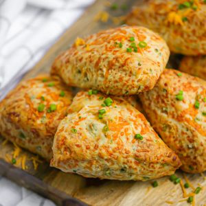 Cheddar Chive Scones on a wood board sprinkled with chives.