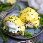 A serving of Crab Eggs Benedict on a round blue plate garnished with minced chives.