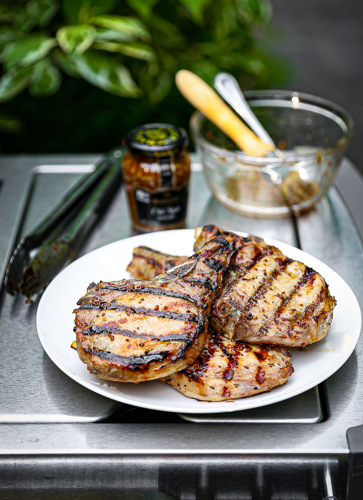 Mustard Glazed Grilled Pork Chops on a white plate on the grill with Maille mustard in the background.