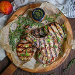 Mustard Glazed Grilled Pork Chops on a round wood serving board with fresh thyme sprigs and Maille mustard on the board.