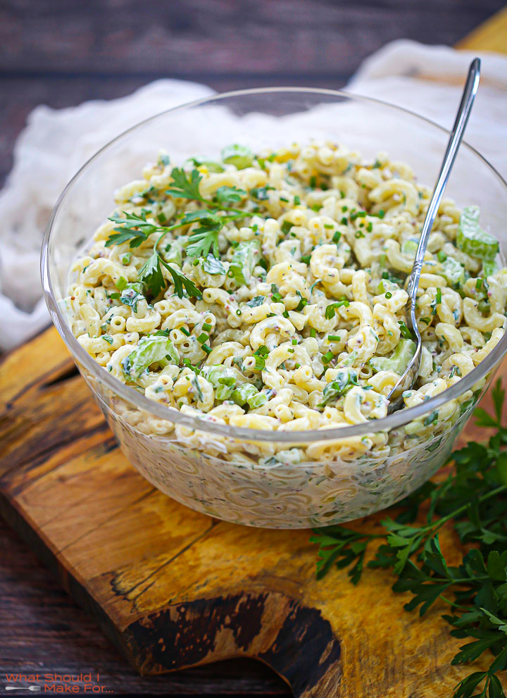 Classic Macaroni Salad in a glass bowl on a wood board garnished with parsley.