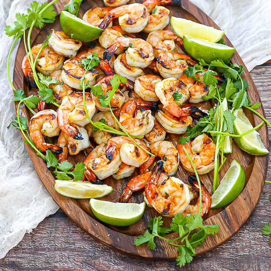 Margarita Grilled Shrimp on an oval wood platter with cilantro,lime wedges and a white table linen.
