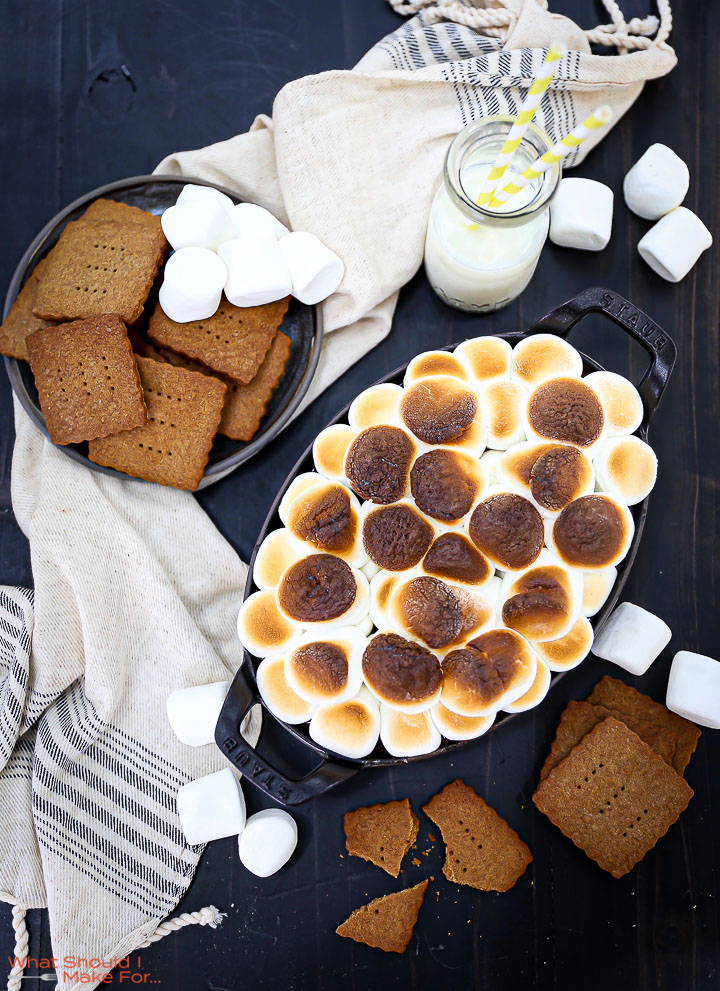 S'mores dip topped with golden brown marshmallows with graham crackers and marshmallows scattered around.