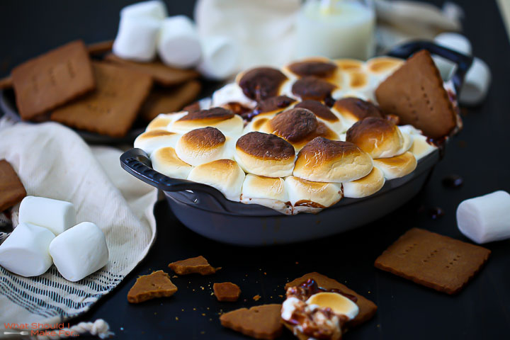 S'mores dip topped with golden brown marshmallows with graham crackers and marshmallows scattered around and a graham cracker stuck in the top.