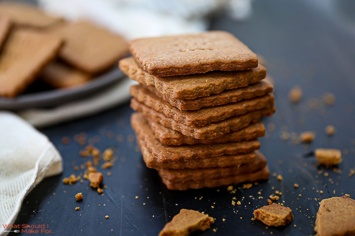 A stack of Homemade Graham Crackers on a black table top with crumbs scattered around.