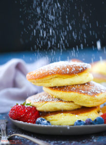 A stack of Fluffy Japanese Pancakes being dusted with powdered sugar.