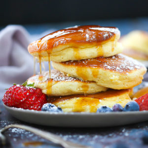 A stack of Fluffy Japanese Pancakes topped with powdered sugar and syrup with berries on the plate.