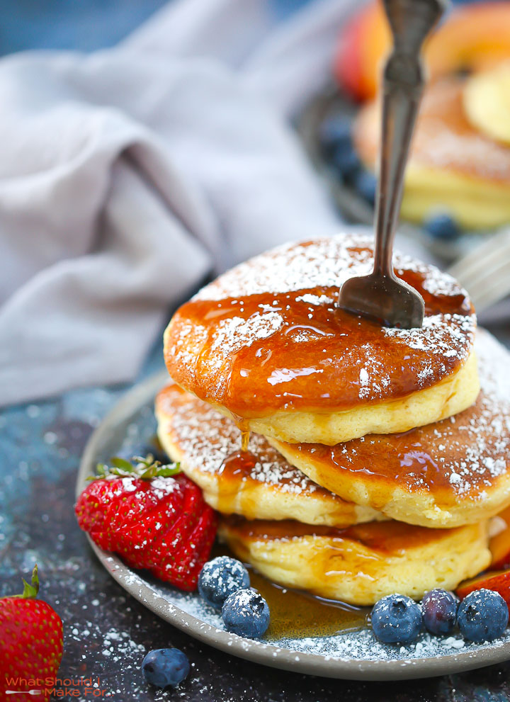 A stack of Fluffy Japanese Pancakes topped with powdered sugar and syrup with a fork stabbed in the top.