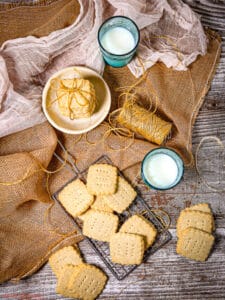 Classic Shortbread Cookies on burlap with a roll of twine, glasses of milk and a white towel.