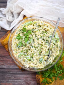 Classic Macaroni Salad in a glass bowl on a wood board garnished with parsley.