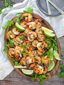 Margarita Grilled Shrimp on an oval wood platter with cilantro,lime wedges and a white table linen.