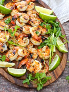 Margarita Grilled Shrimp on an oval wood platter with cilantro,lime wedges and a white table linen.