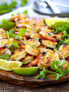 Close up of Margarita Grilled Shrimp on an oval wood platter with cilantro,lime wedges and a white table linen.