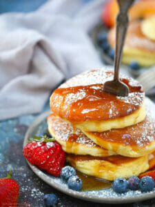 A stack of Fluffy Japanese Pancakes topped with powdered sugar and syrup with a fork stabbed in the top.