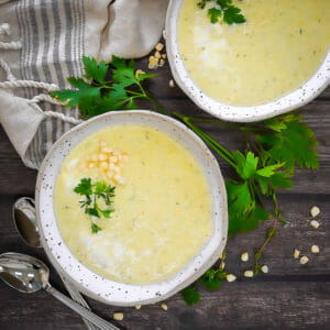 Two bowls of summer corn soup garnished with fresh parsley and a sprinkle of corn.