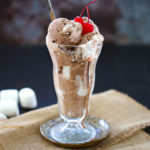 Chocolate Marshmallow Swirl Ice Cream in a tall glass dish topped with cherries.