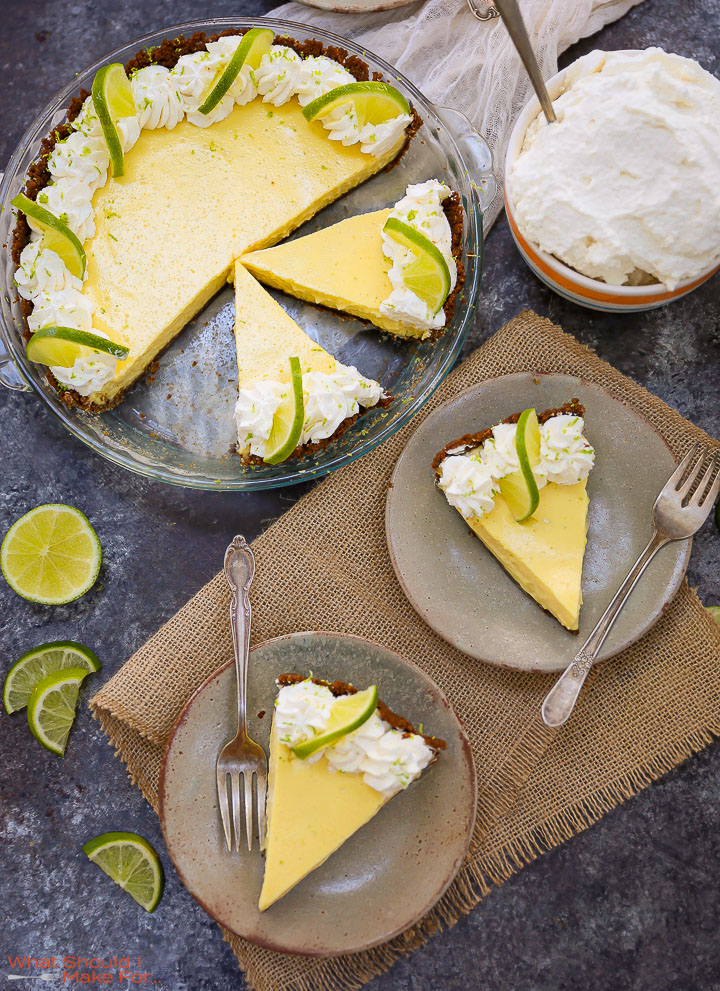 Two slices of Key Lime Pie on plates with the cut pie and bowl of whipped cream on the table.