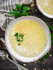 Two bowls of summer corn soup garnished with fresh parsley and a sprinkle of corn.