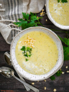 Two bowls of summer corn soup garnished with fresh parsley and a sprinkle of corn.